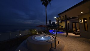 Un espace piscine doté d’un jacuzzi et de chaises longues, offrant une vue sur l’océan au crépuscule.