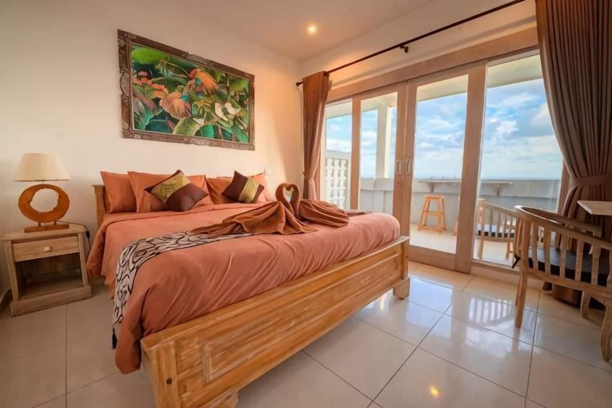 Une chambre à coucher avec un lit, une table de chevet, un tableau, un balcon avec vue et une chaise.