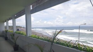 A balcony with potted plants, overlooking a beach with waves and a distant cityscape. -  Sau Bali Beach House Canggu (Pererenan)