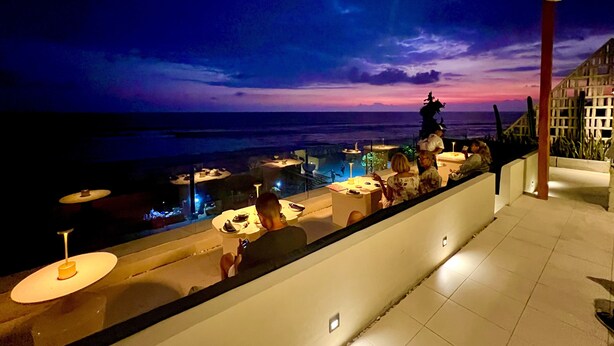 A terrace with tables and chairs overlooking the ocean at dusk. -  Sau Bali Beach House Canggu (Pererenan)