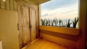 A room with a large window overlooking the ocean, a wooden door with intricate carvings, and a planter with plants on the windowsill. -  Sau Bali Beach House Canggu (Pererenan)
