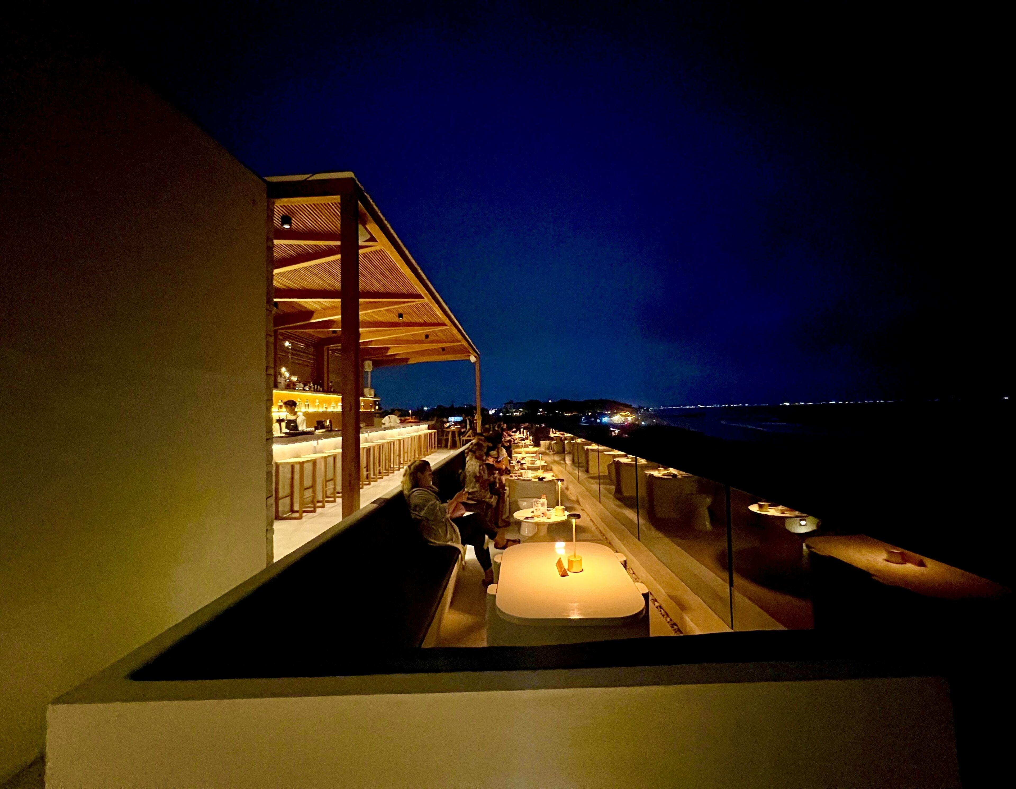 Een terras met een bar en uitzicht op de oceaan in de nacht.