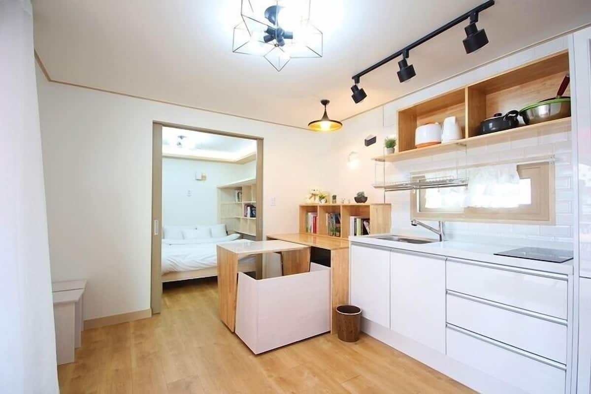 A modern kitchen with white cabinets, a wooden countertop, and a built-in oven. There is a small wooden stool and a trash can in the corner.