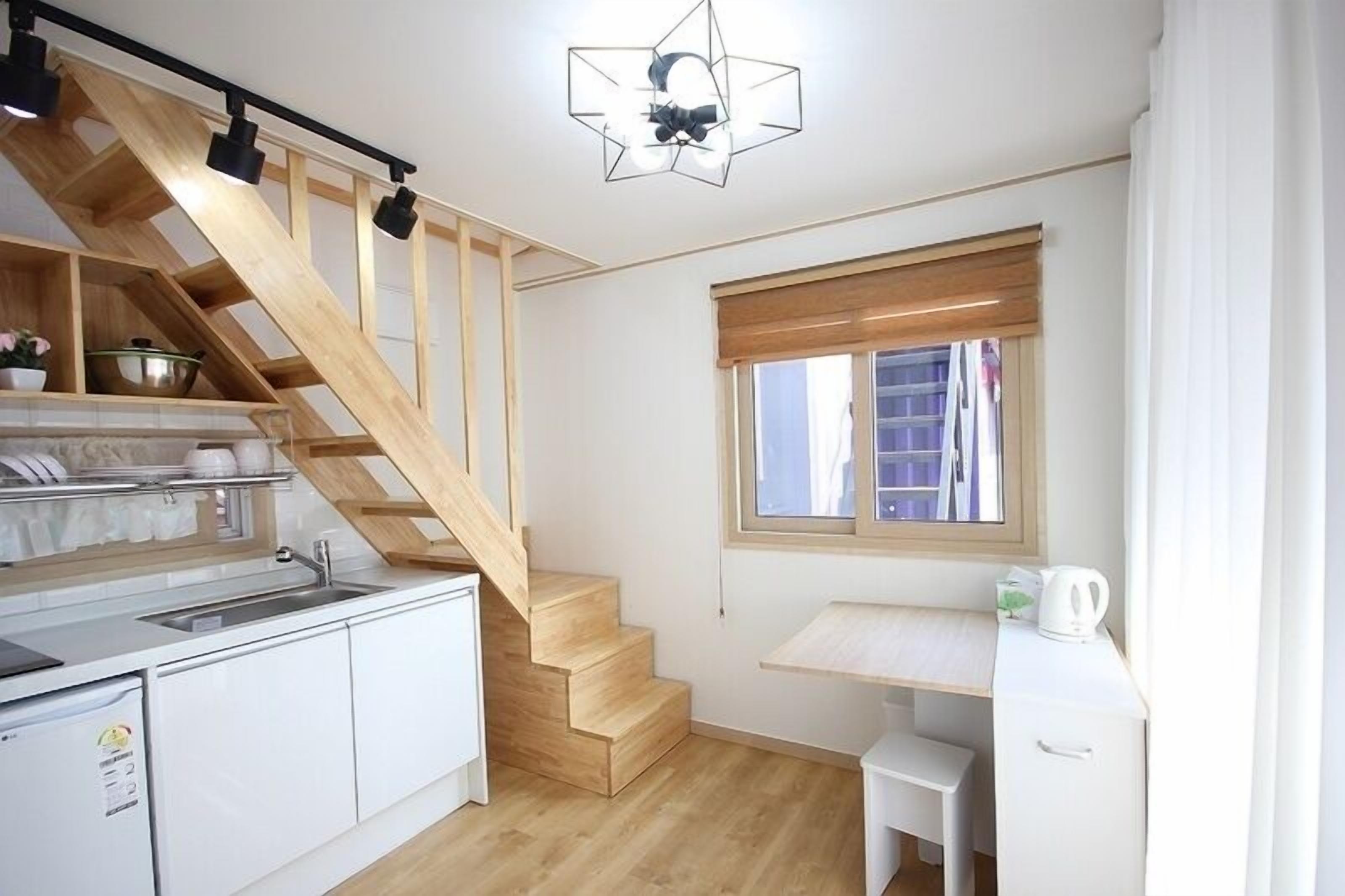 Eine kompakte Küche mit Holztreppe, einem Fenster mit Jalousien und einer kleinen Schreibtischzeile.