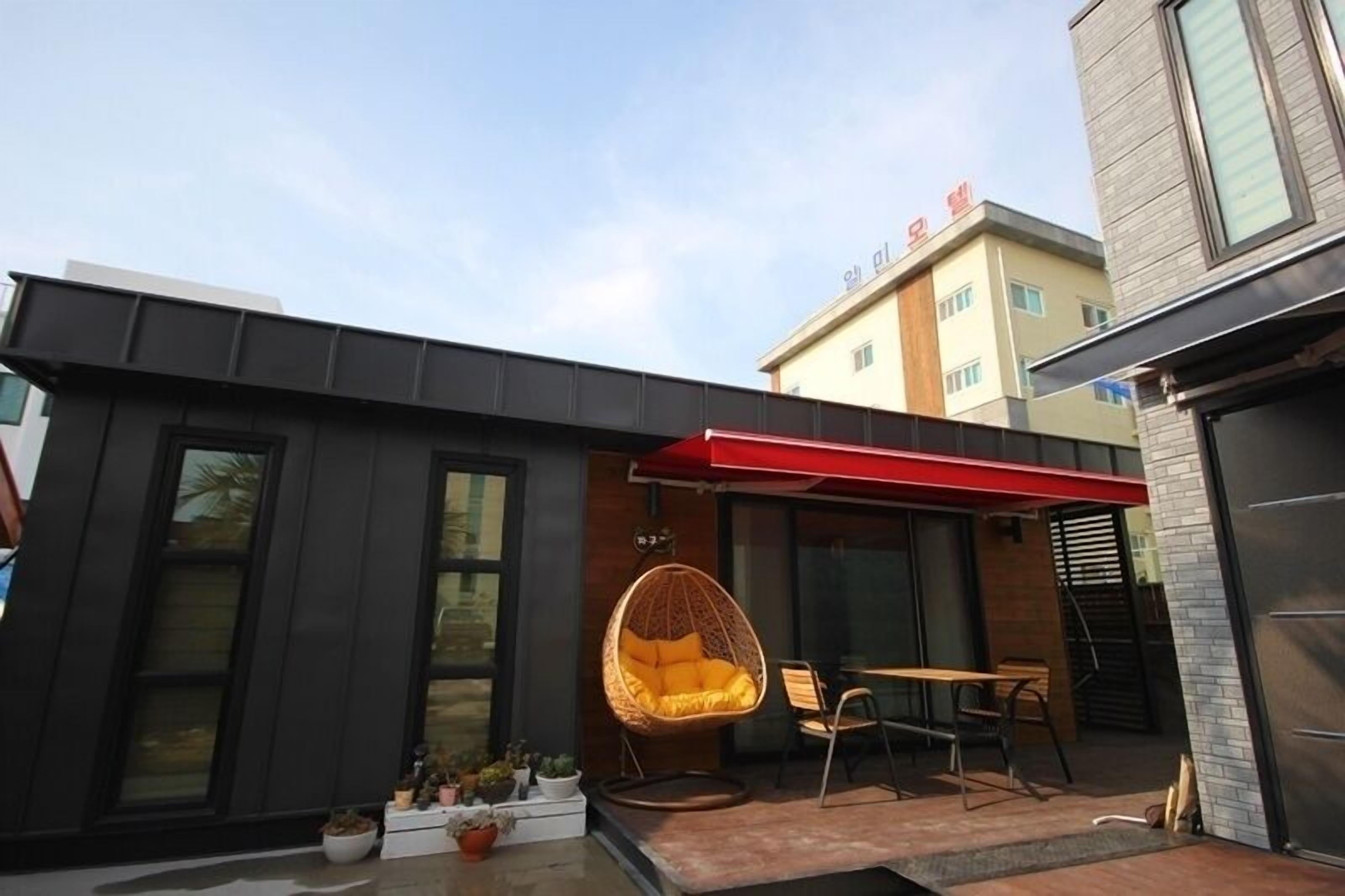 Un edificio moderno con un toldo rojo, una silla colgante y una mesa afuera.