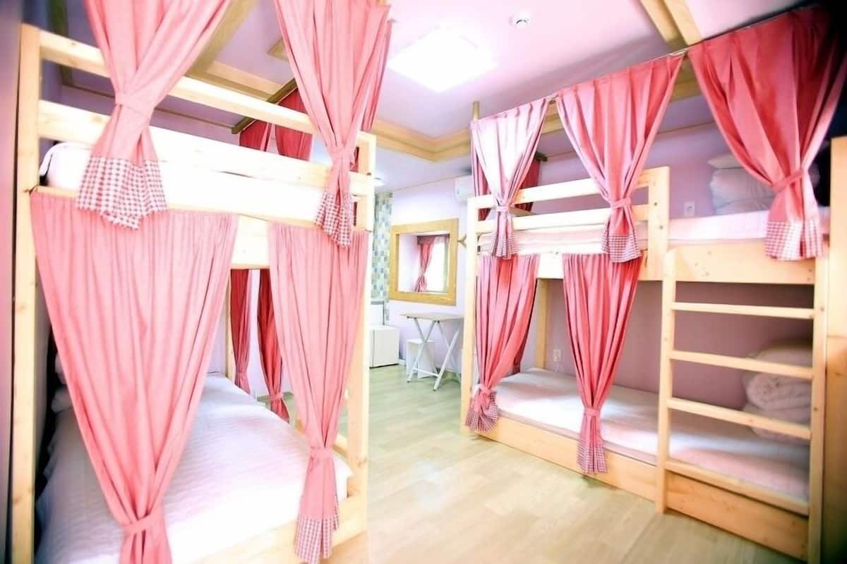 A room with bunk beds, each with pink curtains tied at the head.