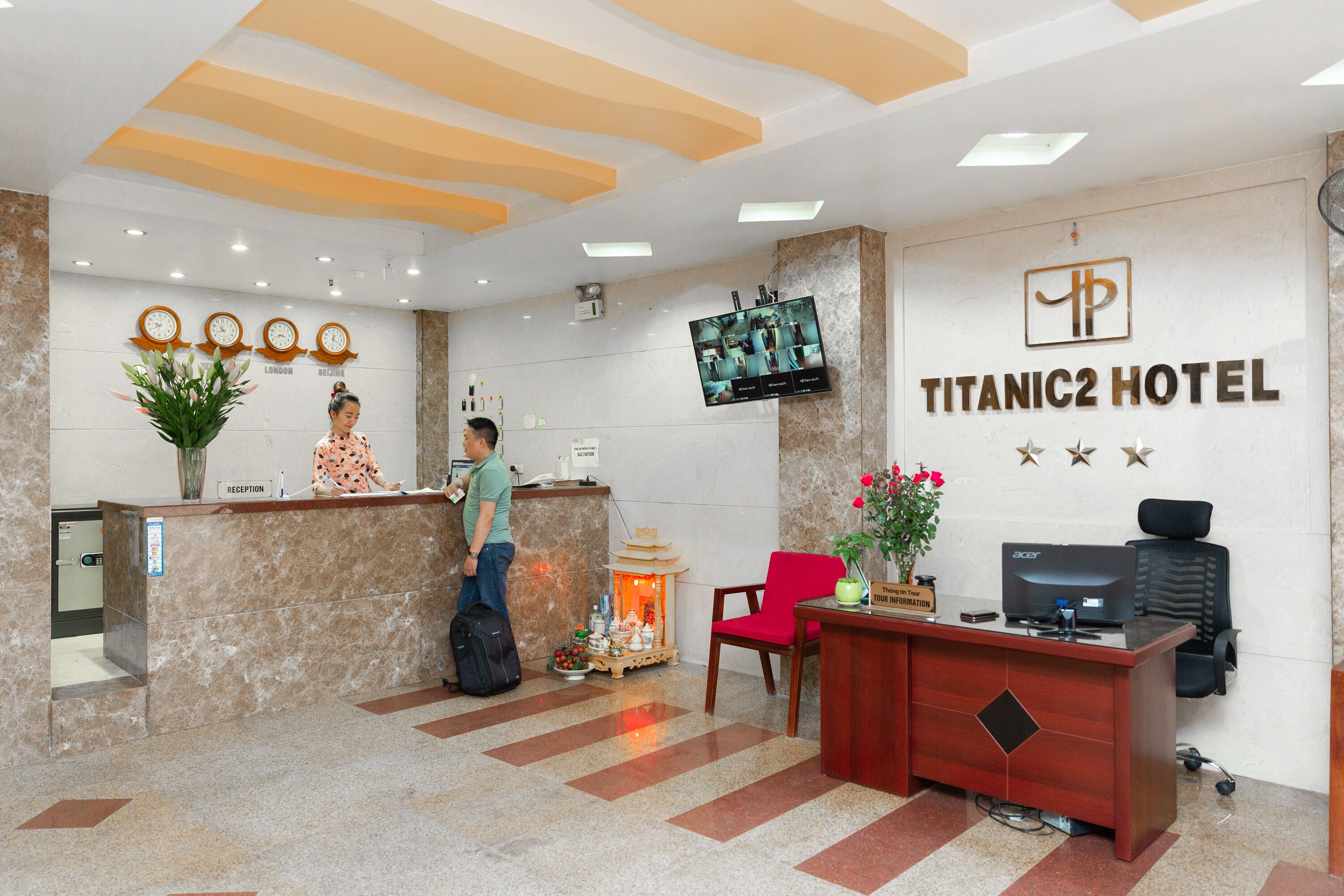 A hotel reception area with a marble reception desk, a television mounted on the wall, and a sign indicating the hotel name.