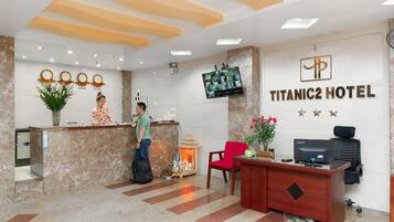 A hotel reception area with a marble reception desk, a television mounted on the wall, and a sign indicating the hotel name.