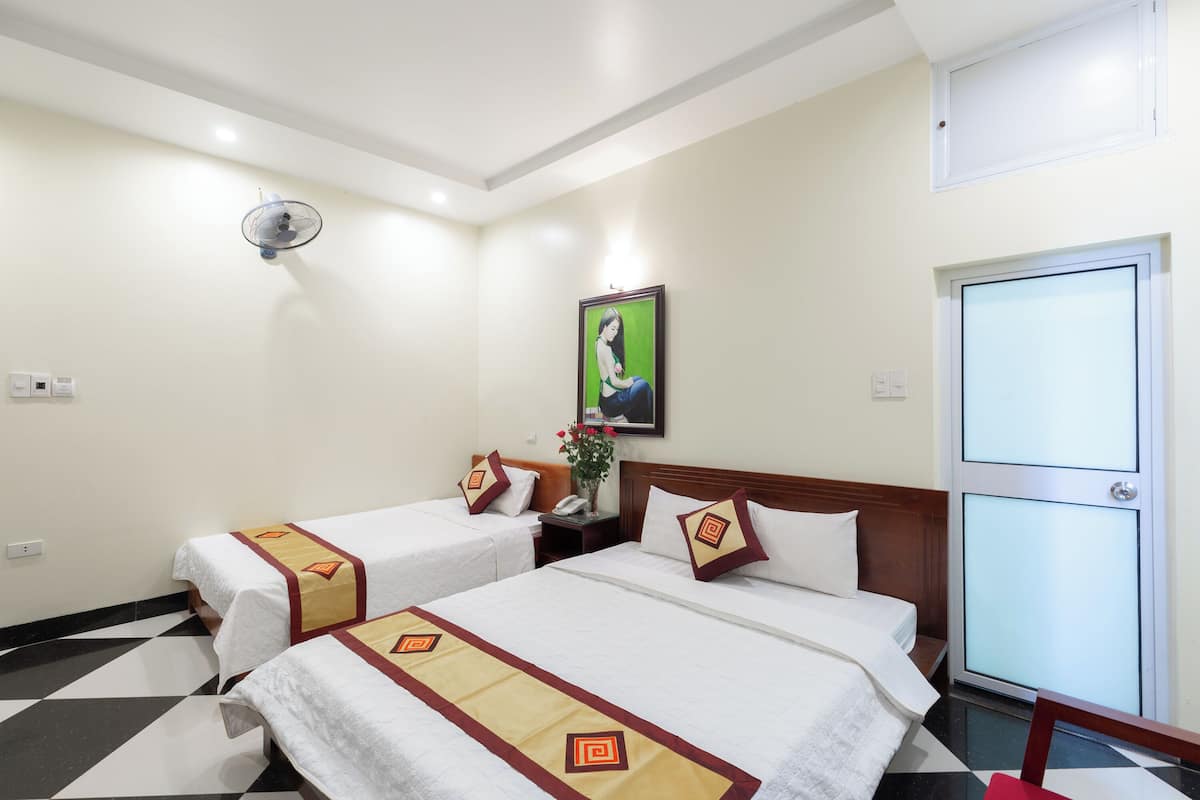 A hotel room with two beds, a nightstand, a wall-mounted fan, a painting, and a door with frosted glass panels.