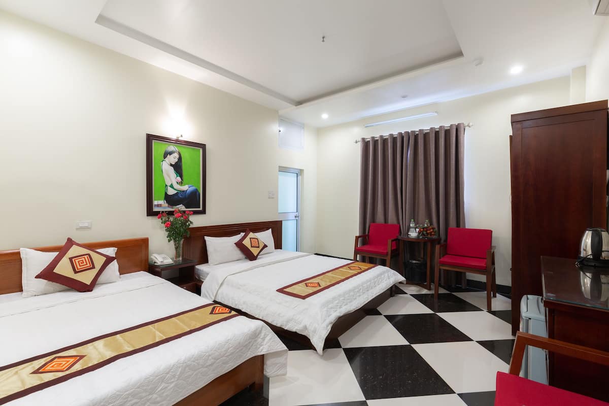 A hotel room with two beds, a desk, a chair, a table, and a painting on the wall.