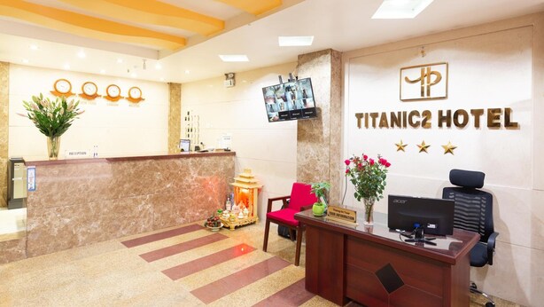 Eine Hotelrezeption mit Marmorablage, einem Bildschirm, einem Schreibtisch mit Computer und einem an der Wand befestigten Schild, das 'Titanic2 Hotel' zeigt.