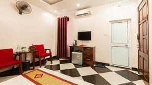 Ein Hotelzimmer mit Schachbrettmuster-Boden, einem Schreibtisch mit Kühlschrank, einem an der Wand montierten Fernseher und einer Tür mit Glasfenster.