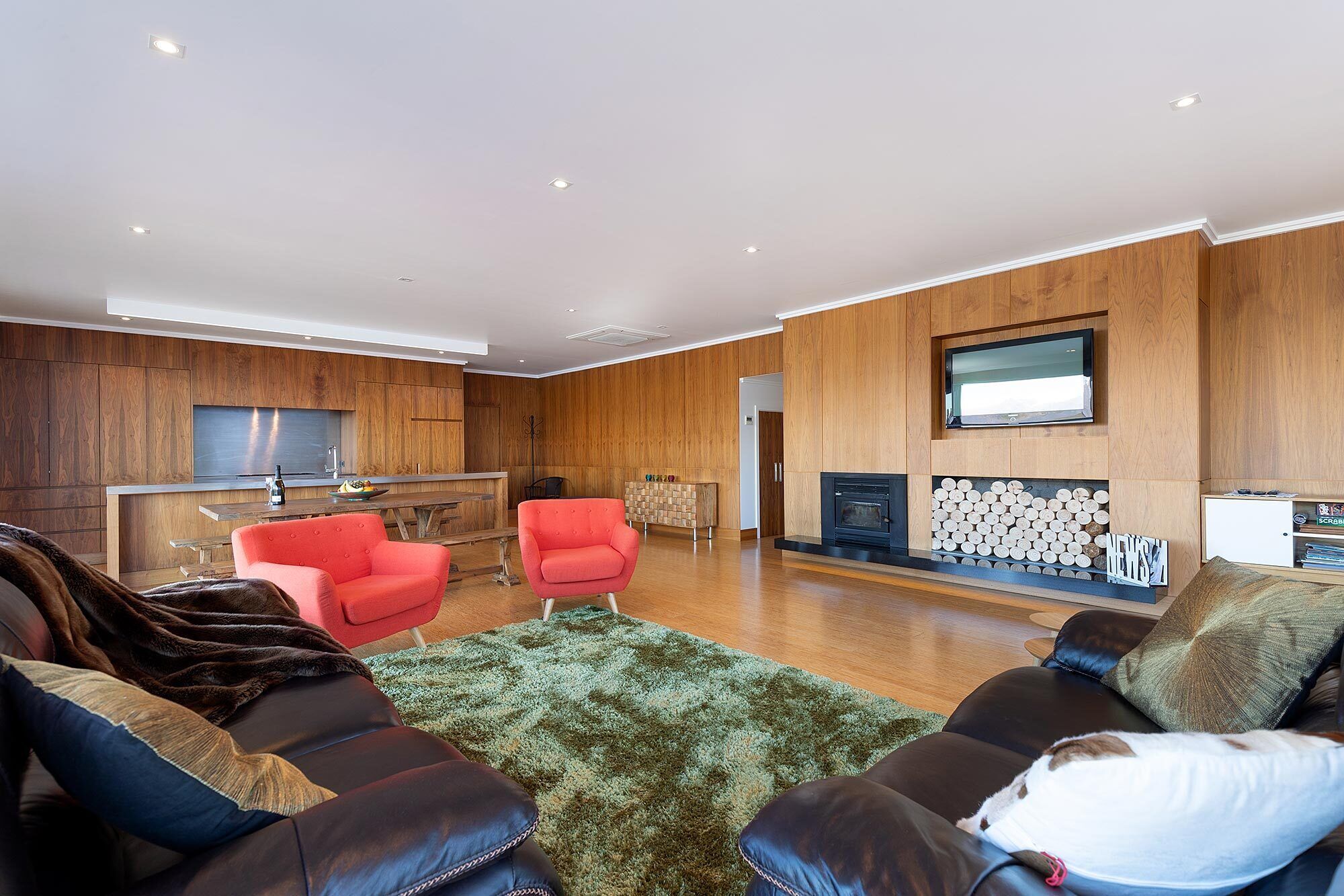 A modern living room with a fireplace, wooden panel walls, and leather sofas.
