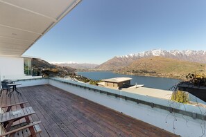 Un balcón con cubierta de madera y una mesa, con vista a un lago y montañas.