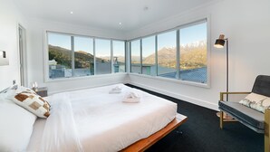 A modern bedroom with a large bed, a desk, and a chair. It features large windows with a mountain view. - Design, Elegance and This Stunning View (Queenstown)