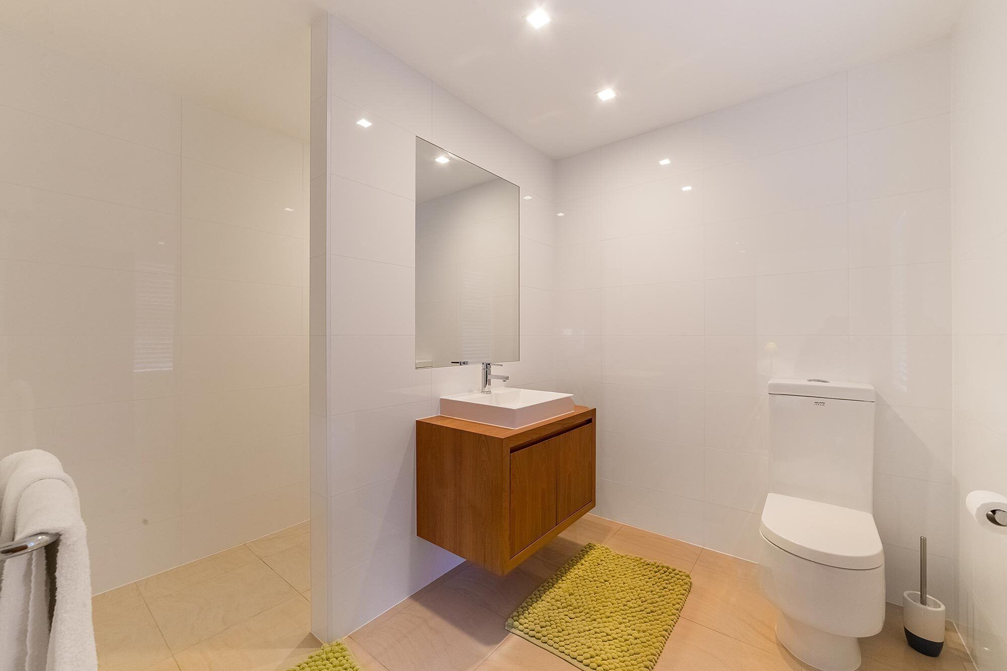 A modern bathroom with a white sink, wooden vanity, a large mirror, and a toilet.