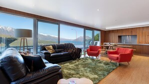 A modern living room with a black leather sofa, red chairs, and a view of mountains through large windows. - Design, Elegance and This Stunning View (Queenstown)