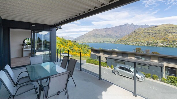 Een modern balkon buiten met een glazen tafel en stoelen, met uitzicht op een meer en bergen.