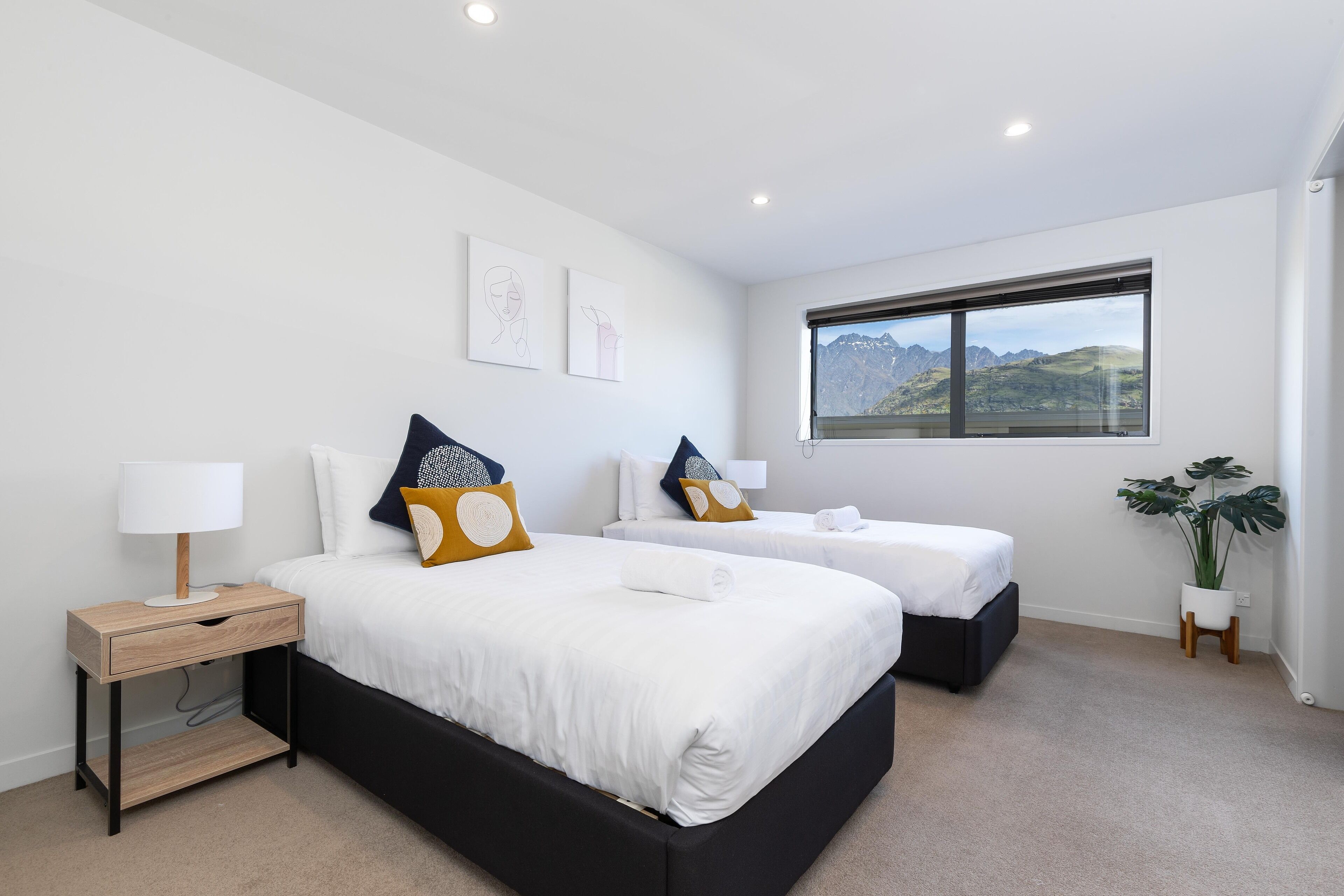 A modern hotel room with two beds, a nightstand, a lamp, and a window with a mountain view.