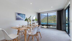 Een moderne eetruimte met een tafel gedekt voor vier personen, een groot raam met uitzicht op bergen en een schilderij aan de muur.