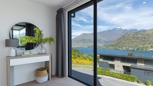 Een kamer met een groot raam, een spiegel, een console met decoratieve voorwerpen, en uitzicht op bergen en een meer.