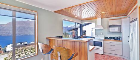 A modern kitchen with wooden accents, a view of a lake, and a bar area with chairs.