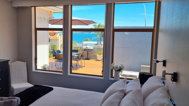 Ein Schlafzimmer mit großem Fenster, Fernseher, Bett und Blick auf eine Außenpatio mit Tisch und Stühlen.