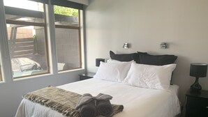Ein ordentlich bezogenes Bett mit weißen Laken und einer braunen Tagesdecke, ein schwarzes Kopfteil sowie ein Nachttisch mit Lampe.