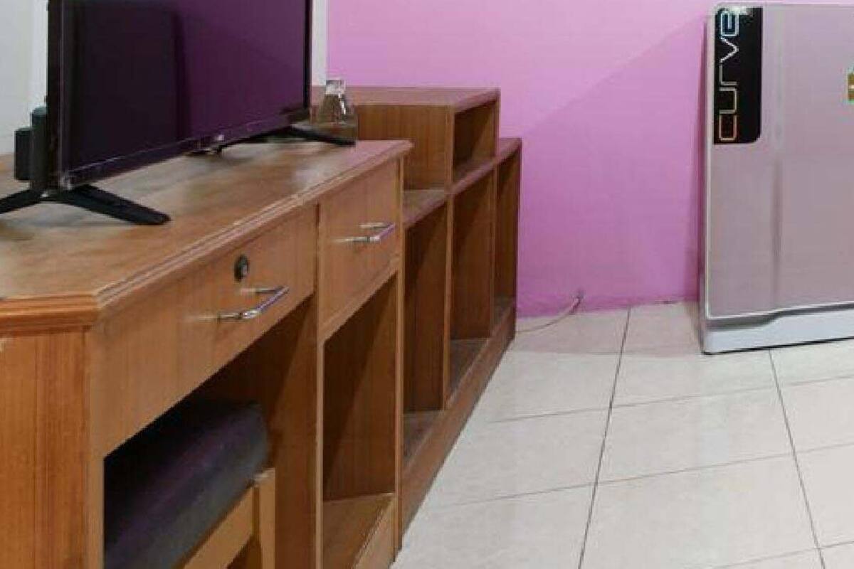 A room with a wooden desk, a flat-screen TV, and a refrigerator.