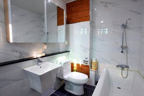 Un baño moderno con un lavabo blanco, inodoro y bañera, paneles de madera en la pared y un espejo grande sobre el lavabo.