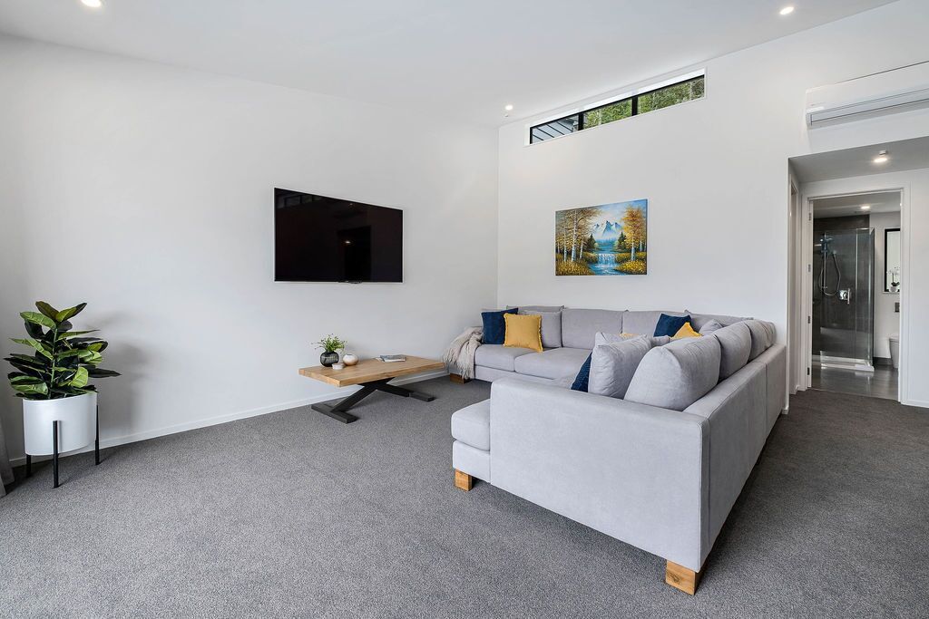 A modern living room with a grey sofa, a coffee table, a flat-screen TV, and a painting on the wall.