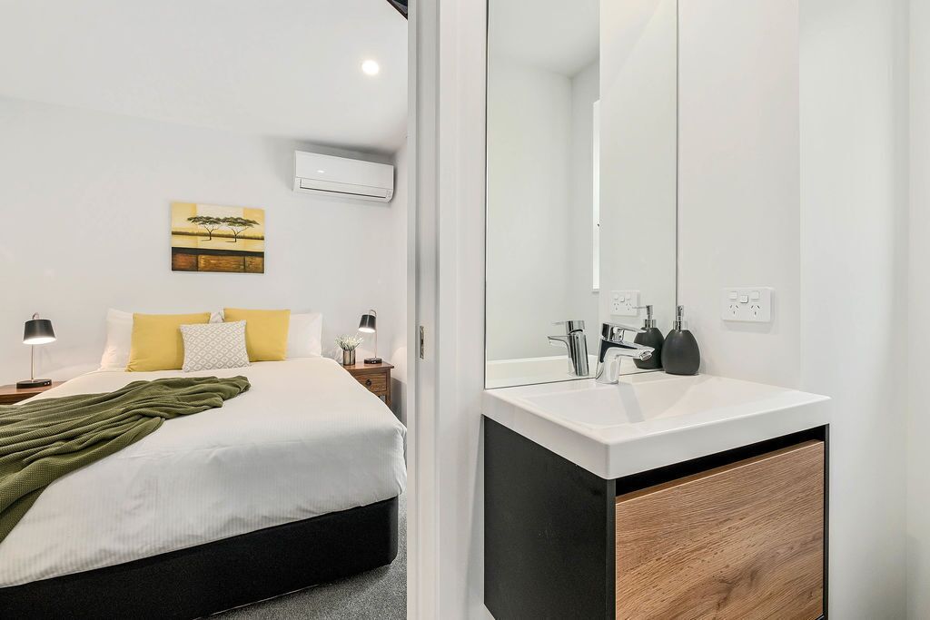 A modern bedroom with a bed, bedside tables, a bedside lamp, a mirror, and a wall-mounted air conditioner.