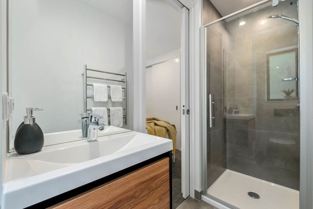 A modern bathroom with a glass-enclosed shower, a white sink with a wooden vanity, and a towel rack with multiple towels.