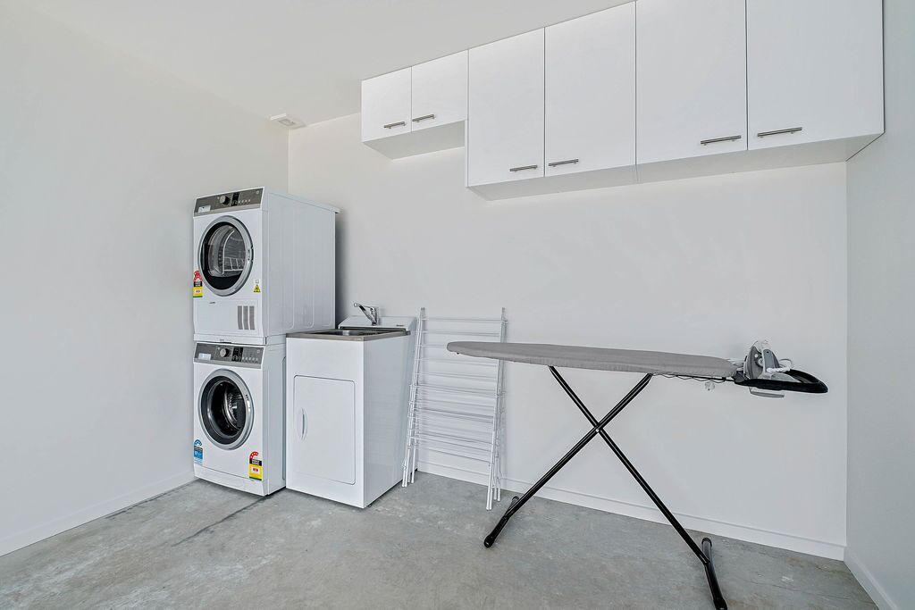 A laundry room with stacked washers and dryers, a drying rack, and an ironing station.
