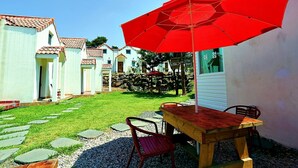 A patio with a wooden table and chairs, a red umbrella, and a stone pathway leading to a building with a tiled roof. - Eltz Town Pension (Jeju City)