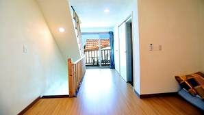 A narrow hallway with wooden flooring, a wooden railing on one side, and a view of a balcony with a tiled roof. - Eltz Town Pension (Jeju City)