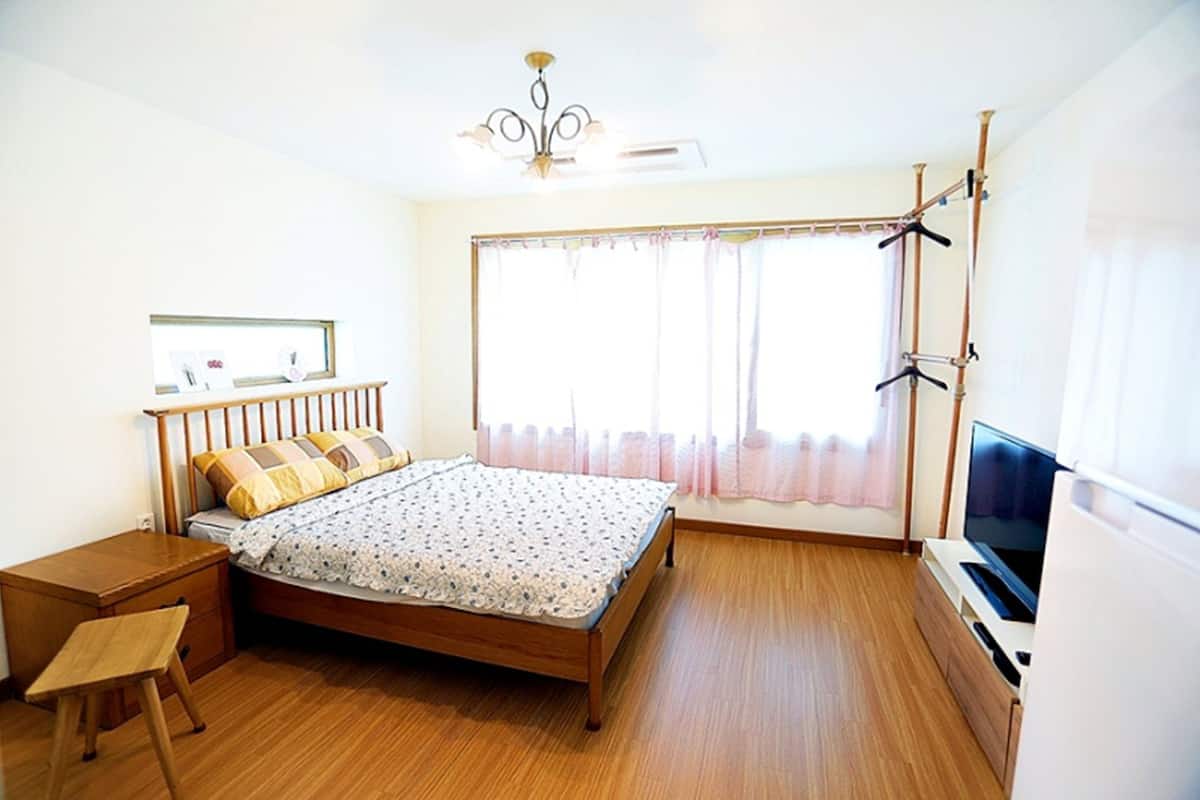 A bedroom with a wooden bed, a small desk, a television, and a window with curtains.