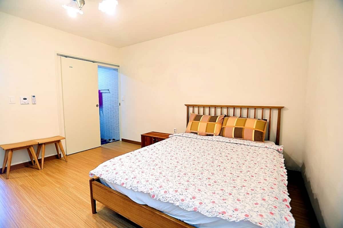 A bedroom with a wooden bed, a bench, and a door leading to another room.