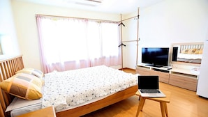 A bedroom with a bed, a TV, a laptop, and a wooden dresser. - Eltz Town Pension (Jeju City)