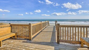 A wooden boardwalk leading to a beach with a wooden bench on the left and a wooden railing on the right.