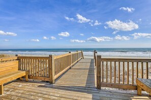 Una passerella in legno che conduce a una spiaggia, con una panchina in legno a sinistra e una ringhiera in legno a destra.
