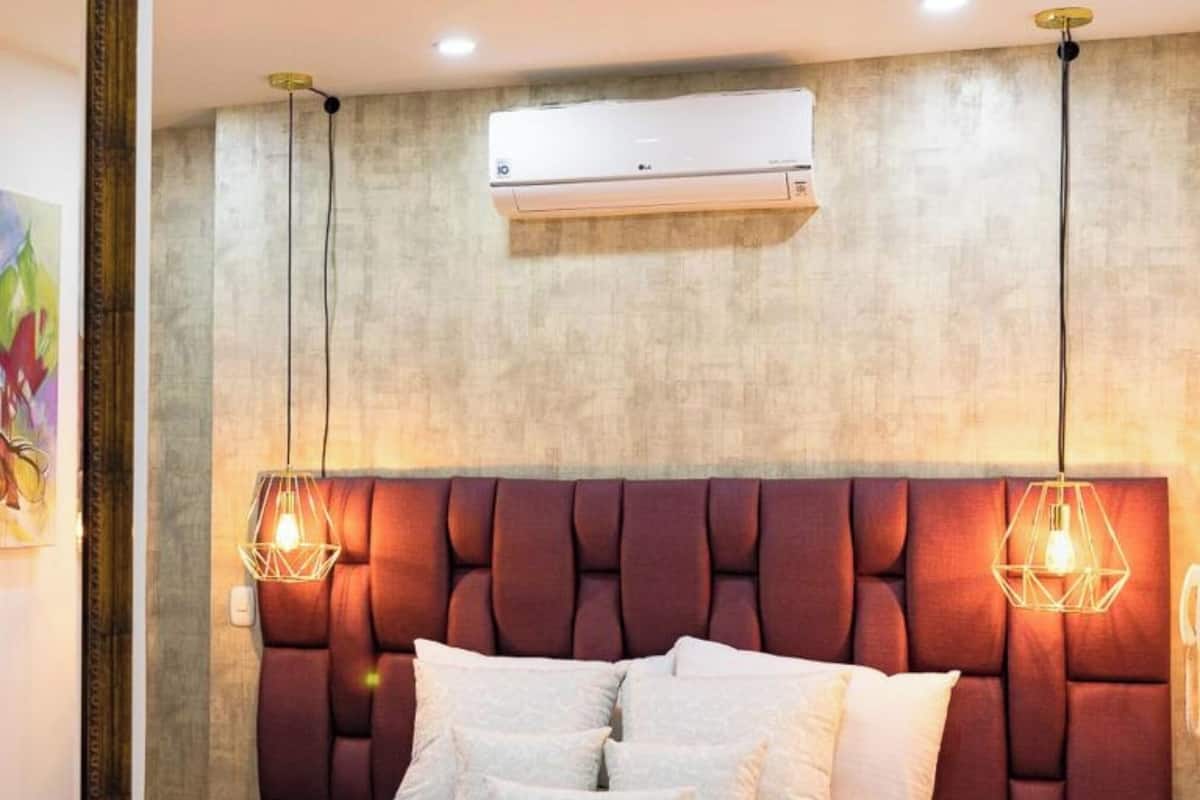 A bedroom with a tufted headboard, a bed with white linens, two bedside tables, and an air conditioning unit above the headboard.