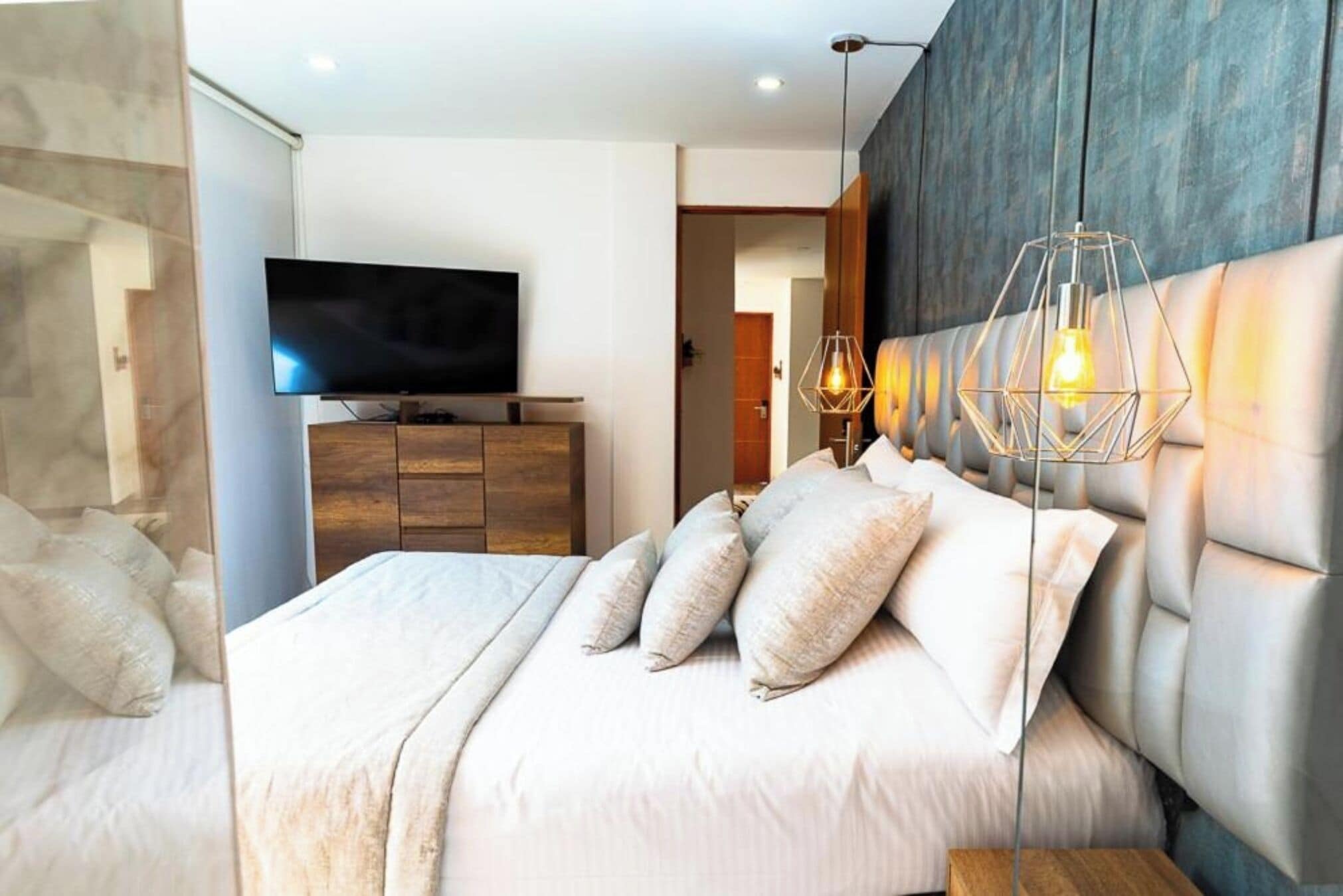 A modern bedroom with a large bed, a flat-screen TV, wooden furniture, and a unique pendant light.