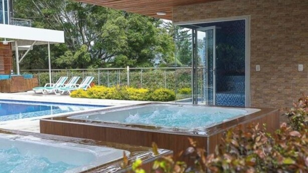 A spa area with a hot tub and a pool, surrounded by lounge chairs and greenery. -  Libertg Hotels Spa Medellin (Copacabana)