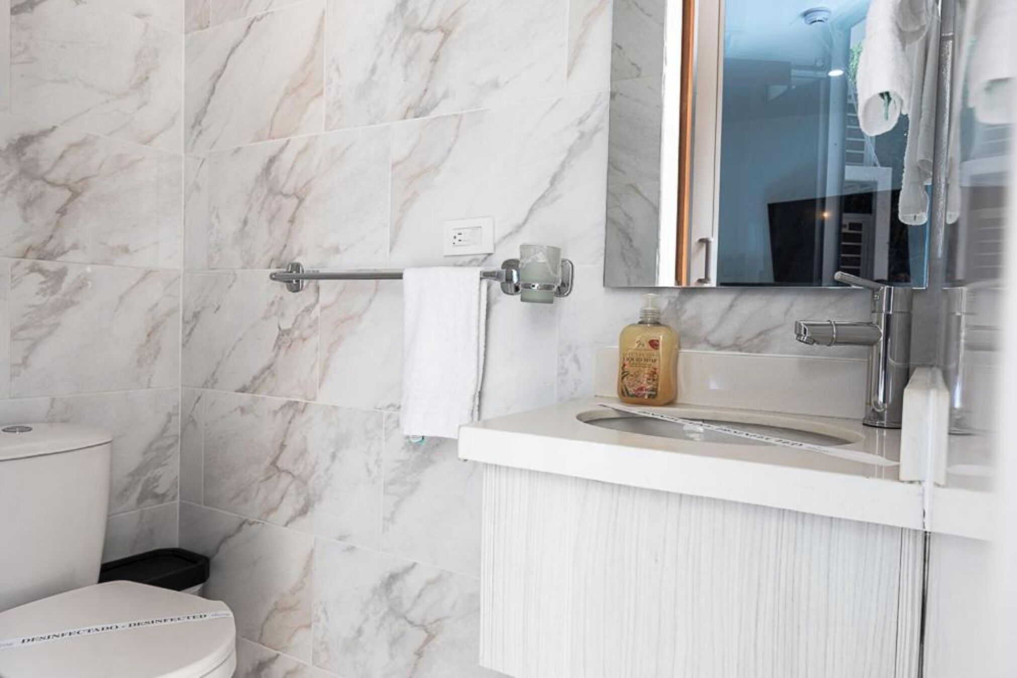 A bathroom with marble tiles, a toilet, a sink with a mirror, and a towel rack.