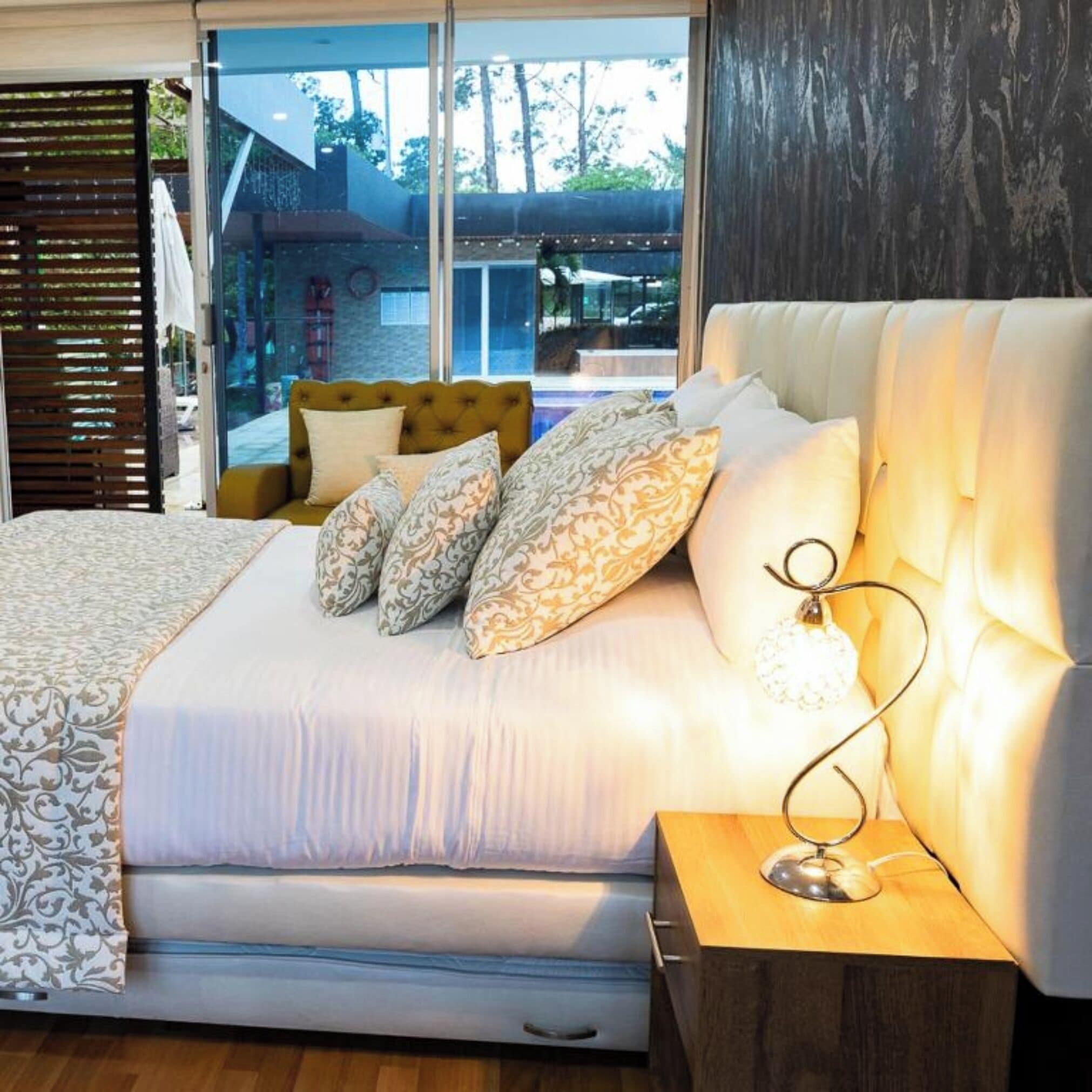 Un dormitorio con una cama grande, una mesita de noche con lámpara y vistas al exterior.