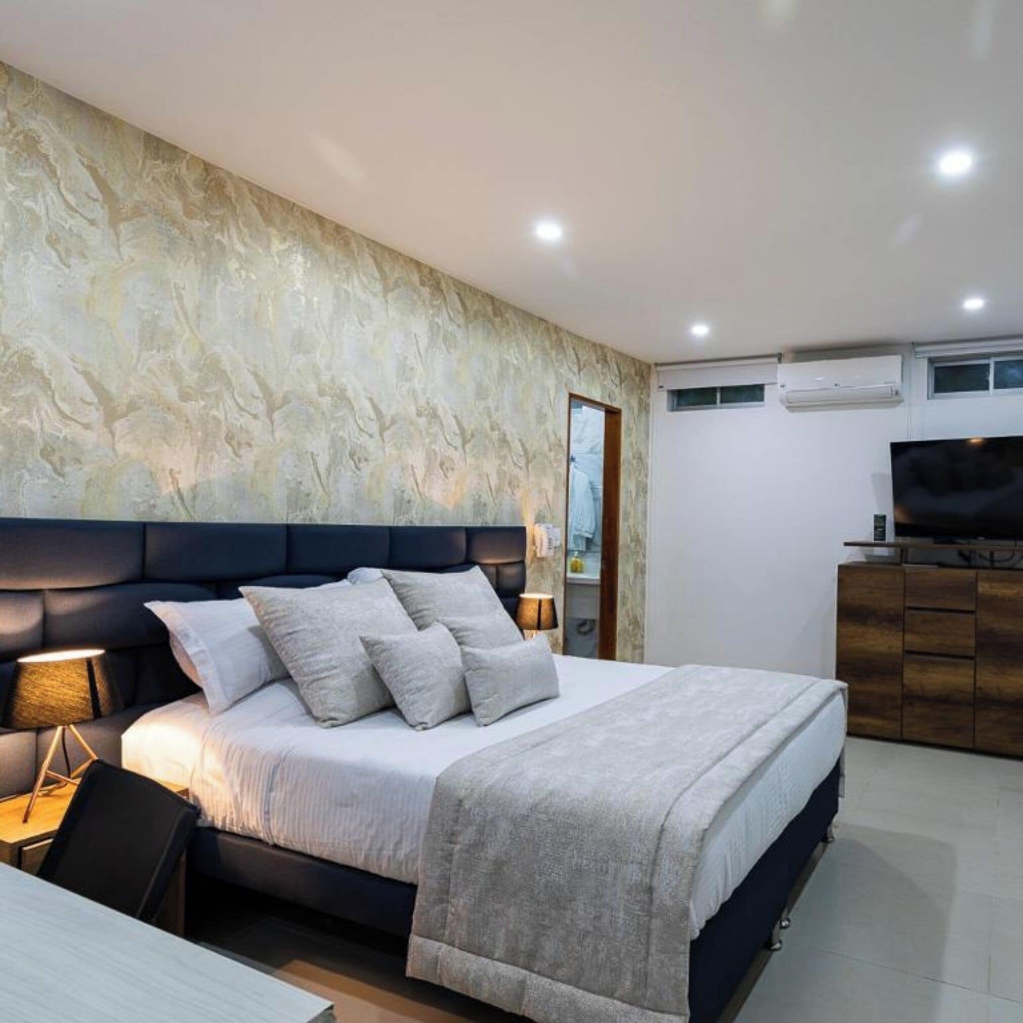 A modern bedroom with a large bed, a nightstand, a TV, and a wardrobe.