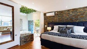 A bedroom with a stone wall, a bed with a dark headboard, and a view of the outside. -  Libertg Hotels Spa Medellin (Copacabana)