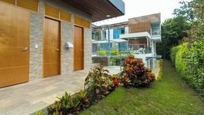 A modern building with large wooden doors, a stone facade, and a well-maintained garden with various plants. -  Libertg Hotels Spa Medellin (Copacabana)
