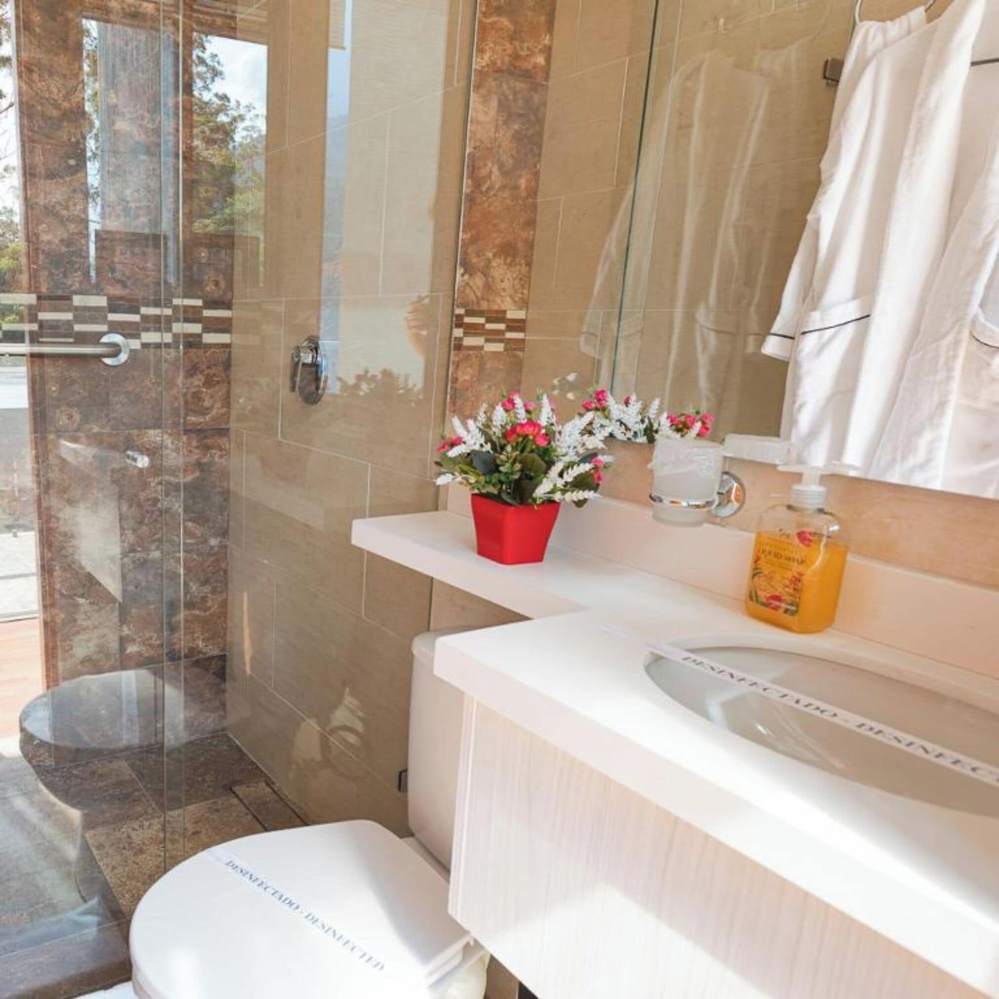 A modern bathroom with a glass shower enclosure, a white sink, a mirror, and a red flower vase.